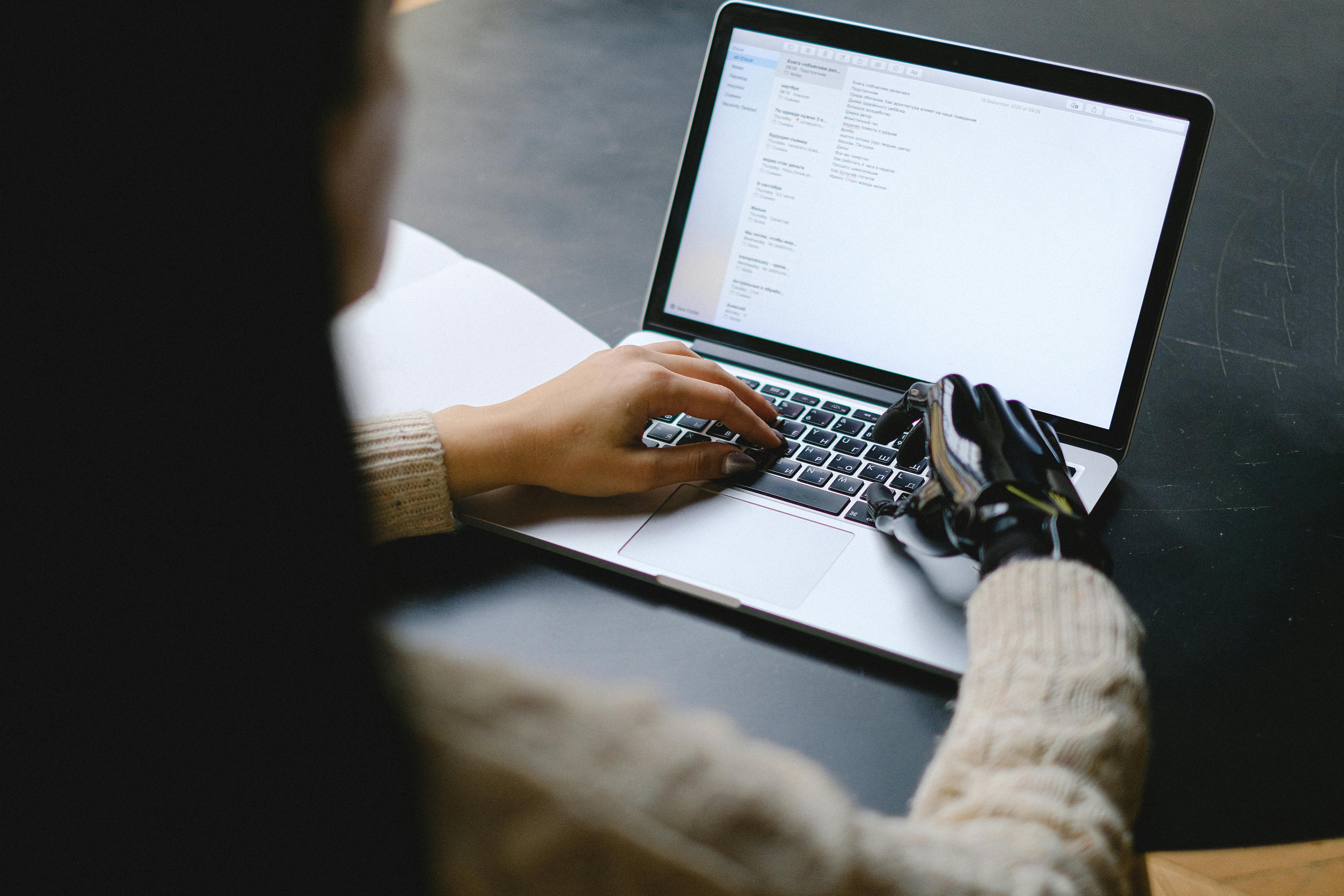 Eine Frau mit einer Handprotese am rechten Arm sitzt an einem Laptop